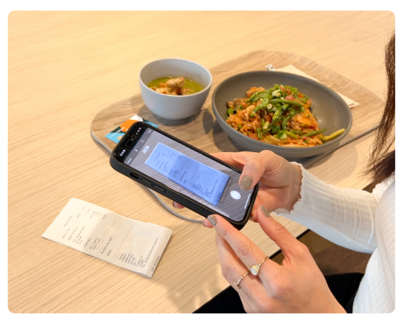 Mitarbeiterin scannt einen Restaurantbeleg mit dem Smartphone während eines Geschäftsessens – digitale Belegerfassung für Bewirtungskosten im Ausgabenmanagement.