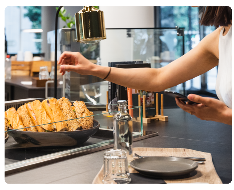 Person nimmt sich Essen in einer Kantine und nutzt das Smartphone – Erfassung von Verpflegungskosten für die digitale Spesenabrechnung mit Mobilexpense