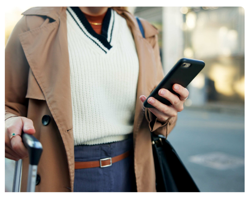 Geschäftsreisende mit Rollkoffer prüft Reisekosten auf dem Smartphone, mobile Reisekostenabrechnung und digitales Spesenmanagement für Unternehmen.